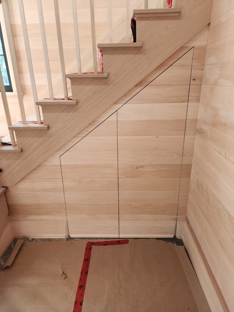 Concealed door under a staircase aligned with horizontal wood wall boards