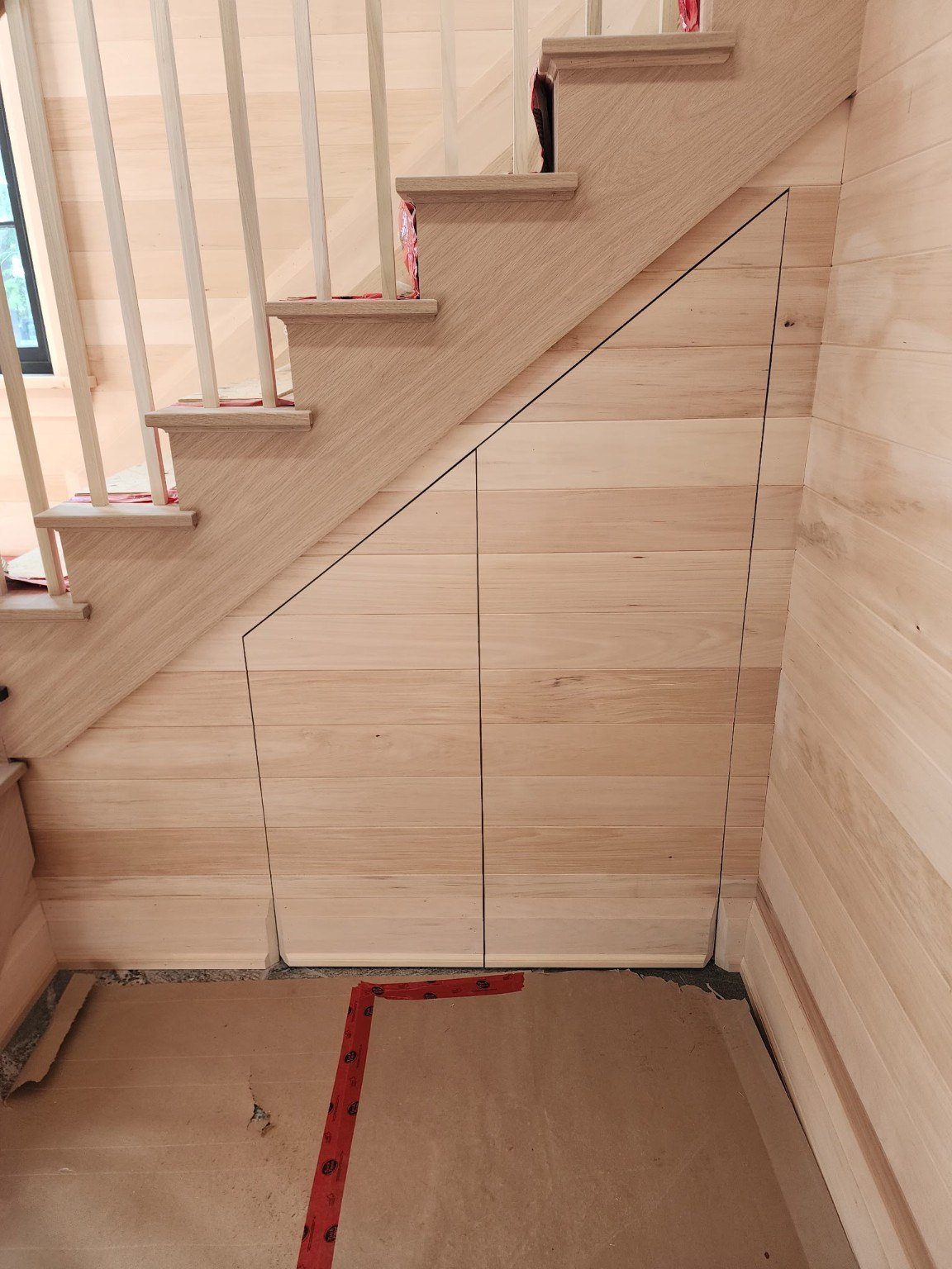 Concealed door under a staircase aligned with horizontal wood wall boards