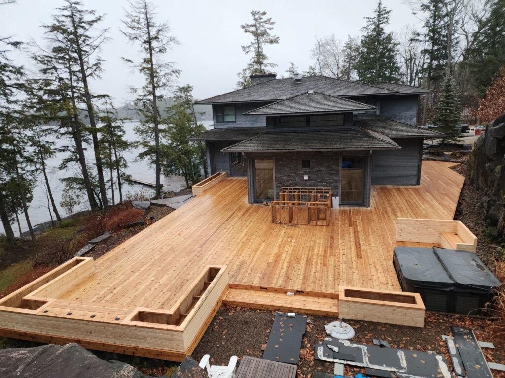 Large wood deck wrapping a waterfront cottage, pictured during construction